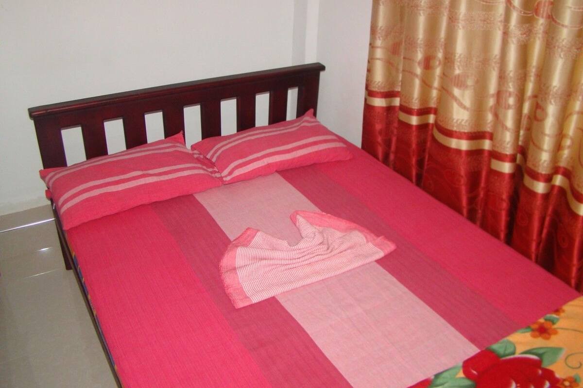A bed with a pink bedspread and pillows, a wooden headboard, and a curtain with a floral pattern.