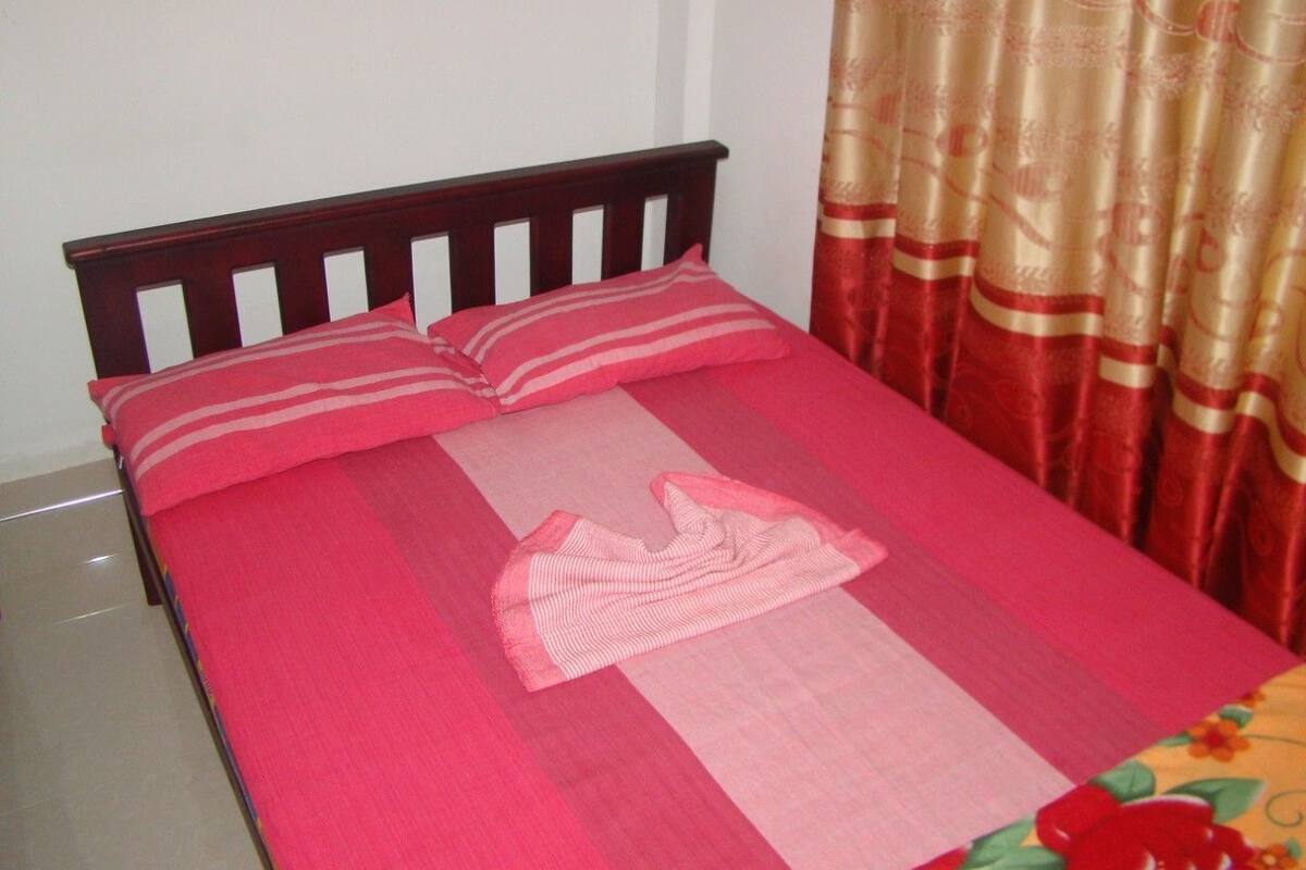 A bed with a red and white striped pillow, a pink bedspread, and a floral curtain.