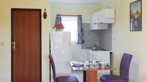 A compact kitchen with a refrigerator, a stove, and a dining table set for four.