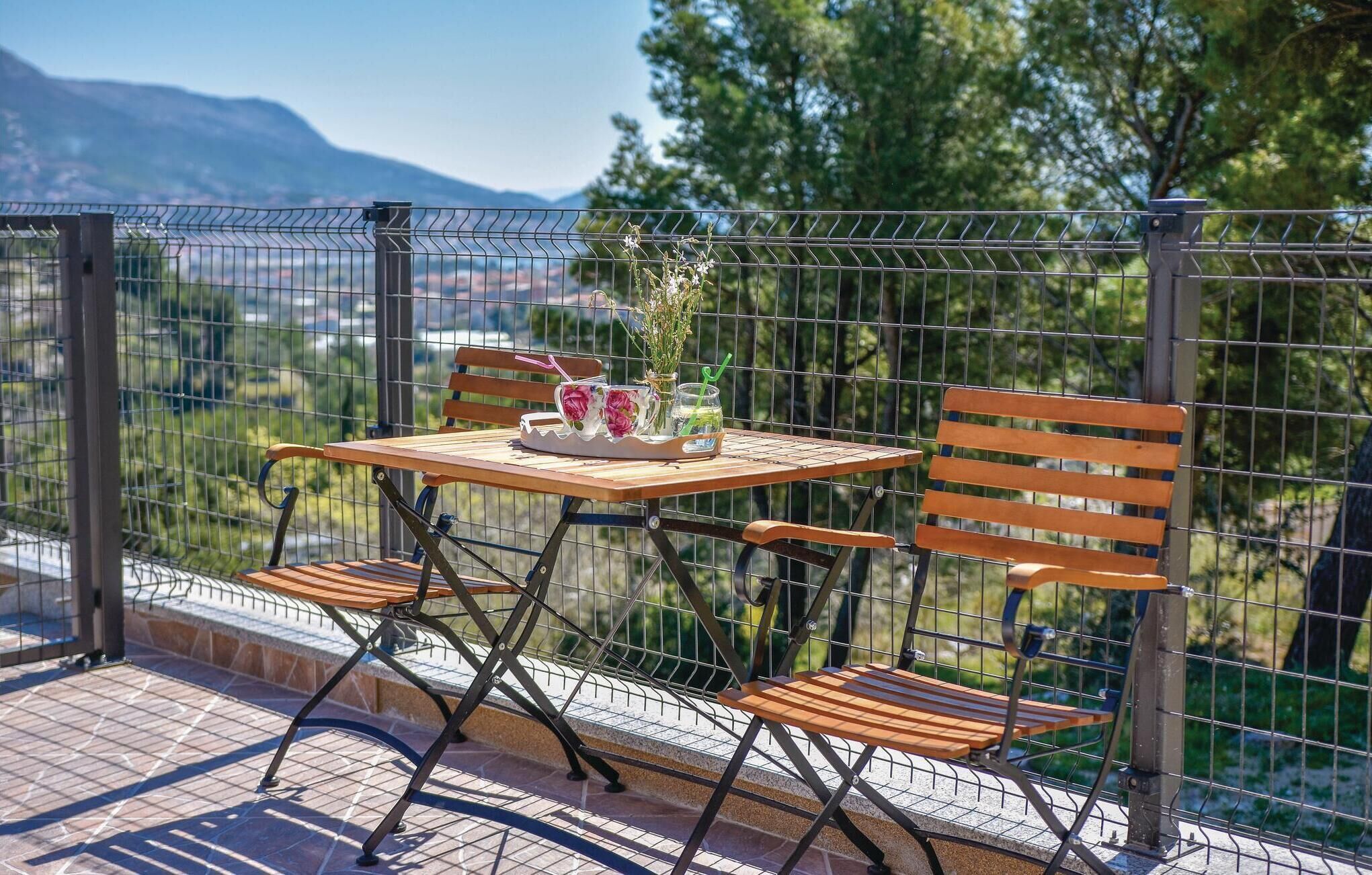 A patio with a table and chairs, a vase with flowers, and a view of greenery and mountains.