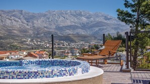 A swimming pool with mosaic tiles, a wooden lounge chair, and a view of mountains in the background. - Cozy home in Split with private swimming pool, can be inside or outside (Split)