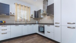 A modern kitchen with white cabinets, a stainless steel oven, and a window with sheer curtains. - Amazing home in Labin (Labin)