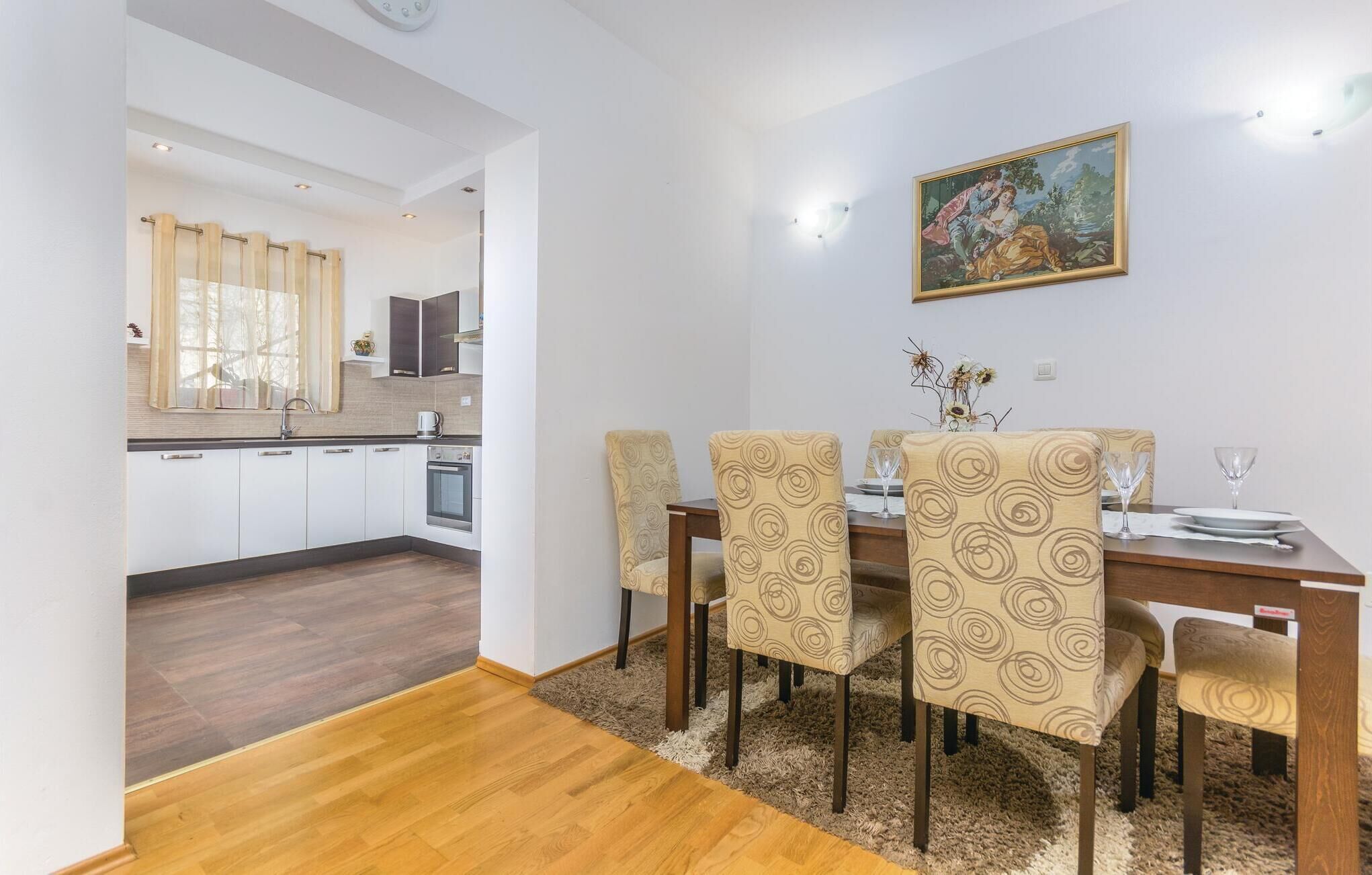 A dining area with a wooden table, four chairs with patterned upholstery, and a painting on the wall.