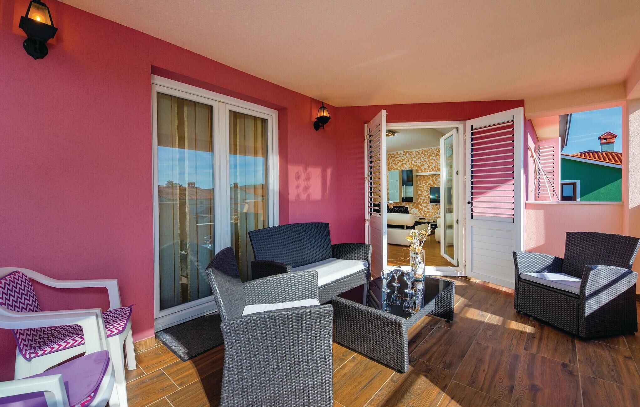 Ein Balkon mit Korbmöbeln, eine Glastür zu einem Zimmer und Blick auf ein Gebäude.