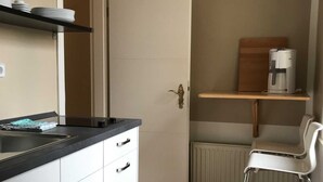 A compact kitchen with white cabinets, a black countertop, a coffee machine, a chair, and a radiator.