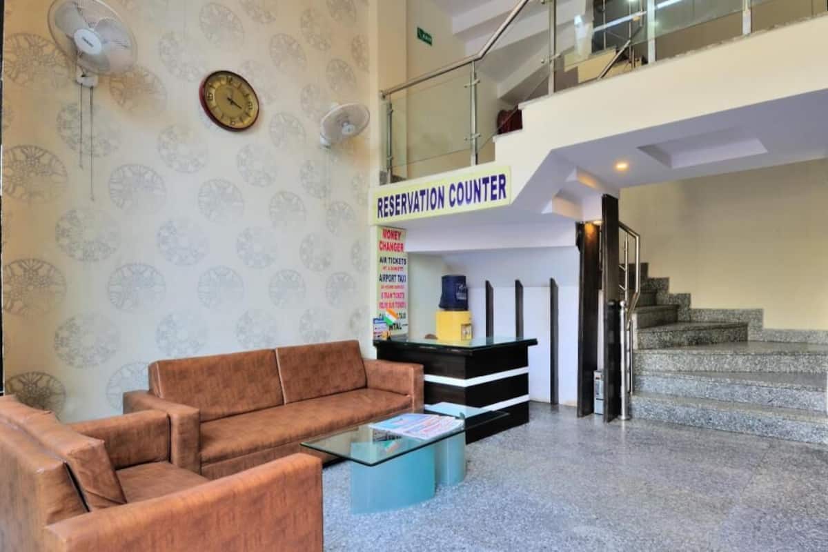 A lobby with a sofa, a glass table, a clock, a reservation counter, and a staircase.