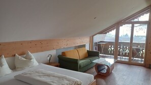 A bedroom with a bed, a green sofa, a wooden headboard, and a large window. - Junior Suite - Grablerhof (Unterroith)