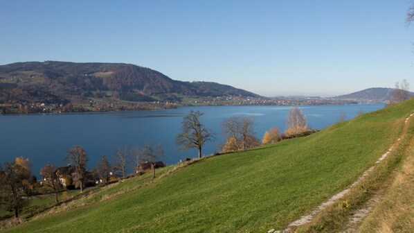 A lake with a path on the right, surrounded by hills and sparse trees.