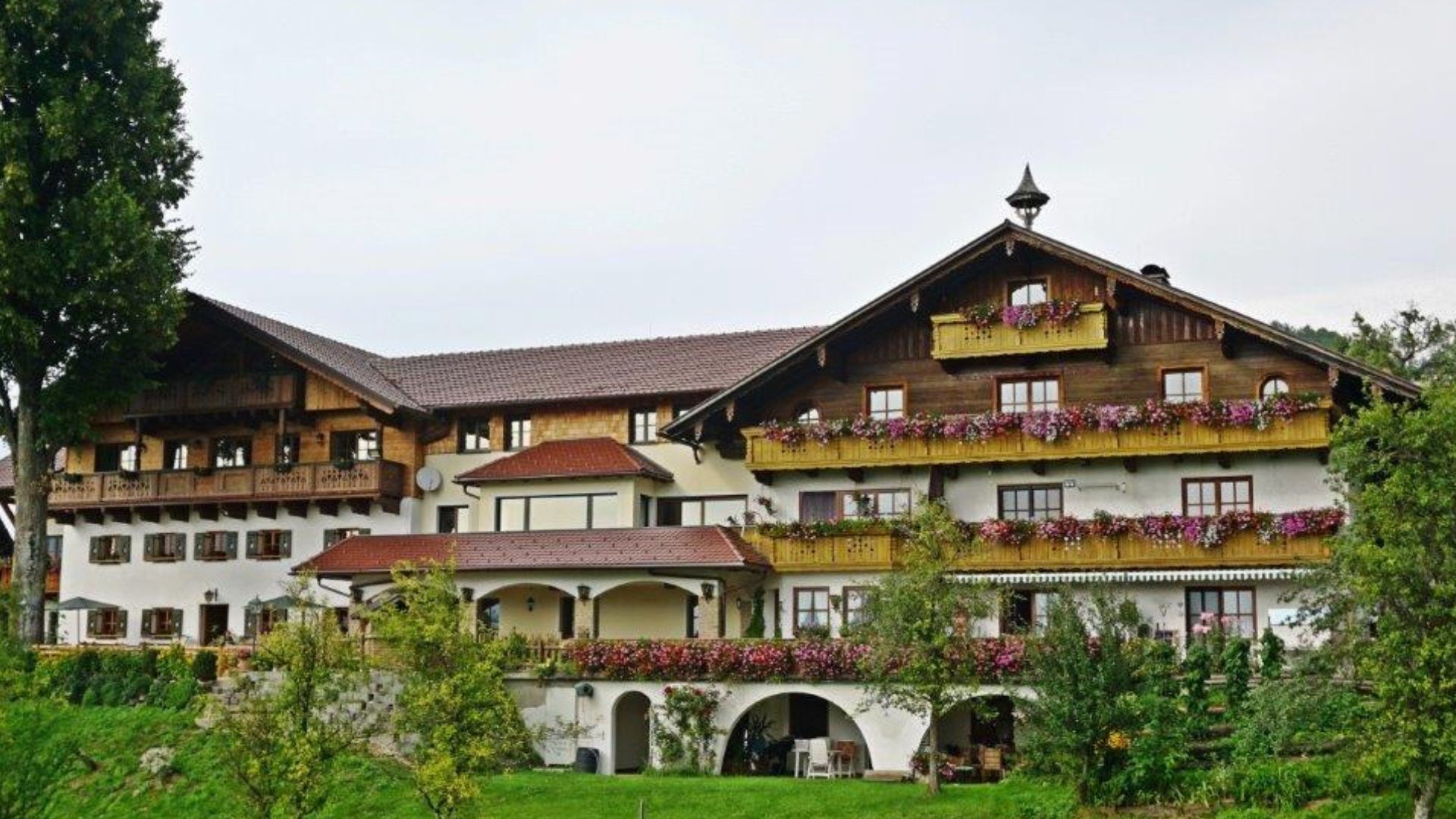 Ein traditionelles Chalet-Hotel mit mehreren Balkonen, einem Garten und Blick auf die Berge.
