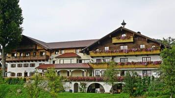 Ein traditionelles Chalet-Hotel mit mehreren Balkonen, einem Garten und Blick auf die Berge.