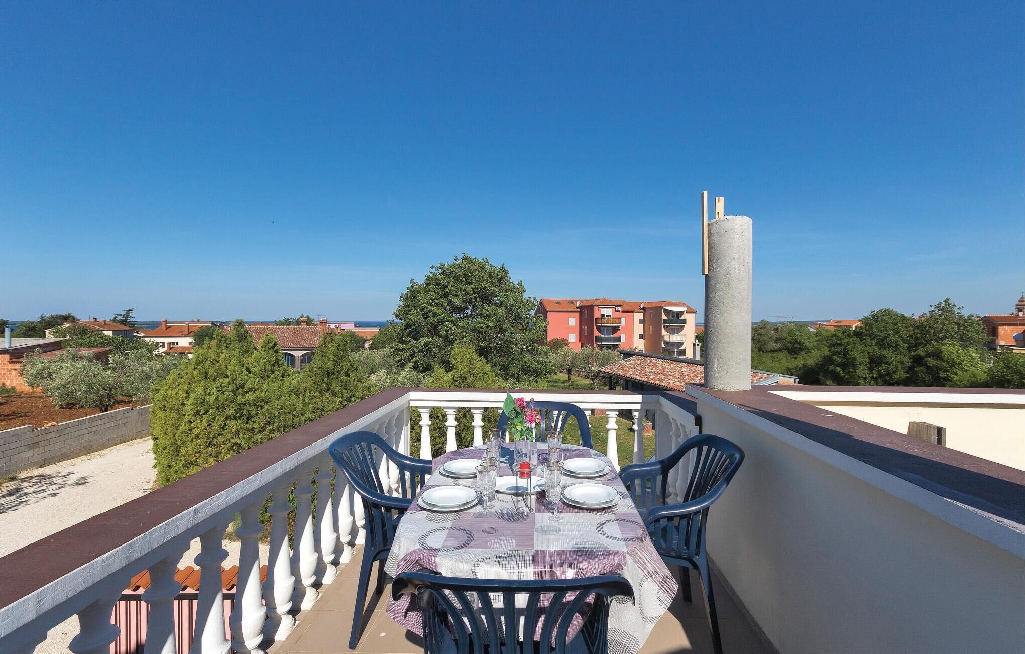 A balcony with a table set for dining, overlooking a residential area with buildings and trees.