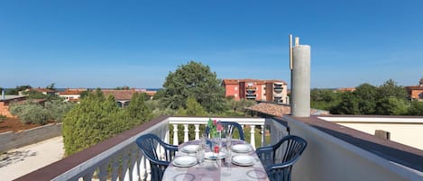 A balcony with a table set for dining, overlooking a residential area with buildings and trees.