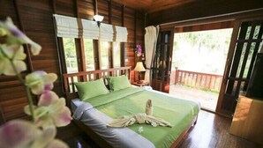 A wooden cabin bedroom with a bed, green bedding, a nightstand, and a window with curtains. - Sasi Resort (Song Phi Nong)