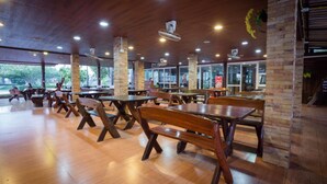 A spacious indoor dining area with wooden tables and benches, large windows, and a high ceiling with recessed lighting. - Sasi Resort (Song Phi Nong)