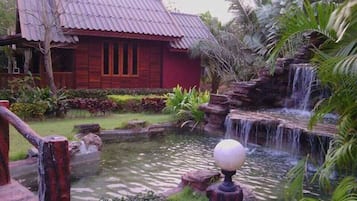 Una casa de madera tradicional con techo rojo, un pequeño estanque y una cascada.