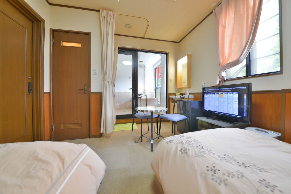 A hotel room with two beds, a television, a desk, and a bathroom visible through an open door.