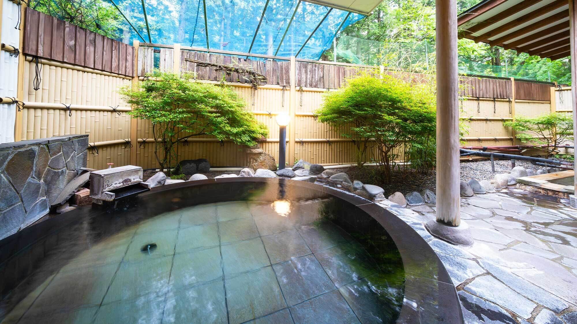 A hot spring bath area with stone flooring, a wooden fence, and bamboo plants.