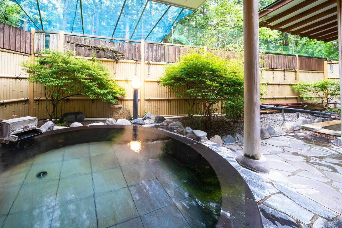 A hot spring bath area with stone flooring, a wooden fence, and bamboo plants.