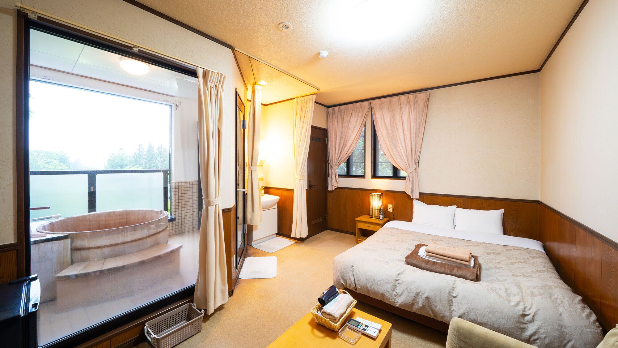 A hotel room with a large window, a bed, a bedside table, a nightstand, and a small seating area with a chair.