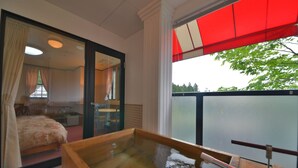 A room with a large glass door leading to a balcony, a wooden bathtub, and a view of trees. - Hotel Euro City (Nikko)