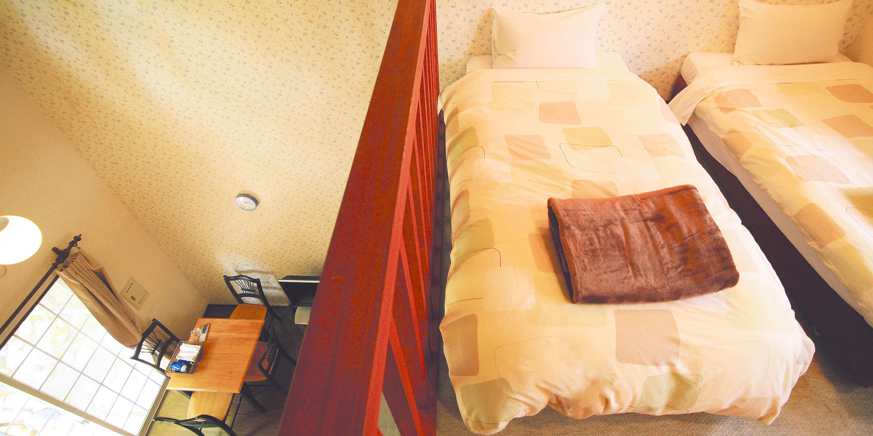 A room with two beds, a wooden desk, and a window with curtains.
