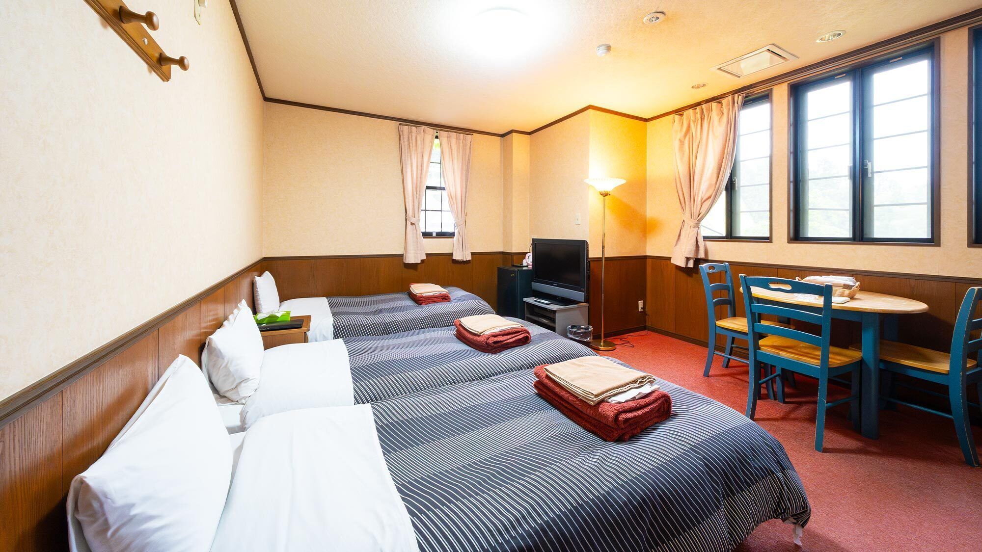 A hotel room with two beds, a TV, a desk with chairs, and a window with curtains.