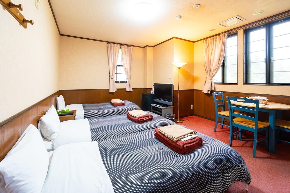 A hotel room with two beds, a TV, a desk with chairs, and a window with curtains.