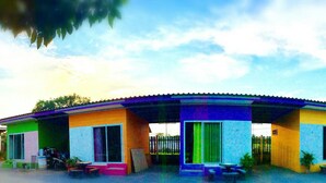 Un edificio colorato con diverse porte e finestre, una zona esterna coperta con tavoli e sedie, e un cielo sereno sullo sfondo.