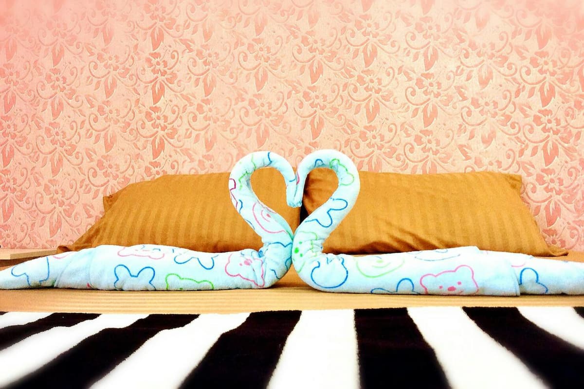 Una cama con una toalla dispuesta en forma de corazón y un papel tapiz estampado al fondo.