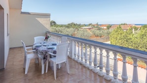 Un balcone con un tavolo apparecchiato per due, sedie bianche e vista sul mare e sugli edifici.
