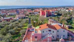 Una zona residenziale costiera con case dai tetti rossi, un edificio rosso al centro e vista sul mare.