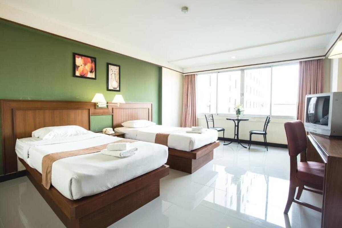 A hotel room with two beds, a desk with a TV, a small table with chairs, and artwork on the walls.