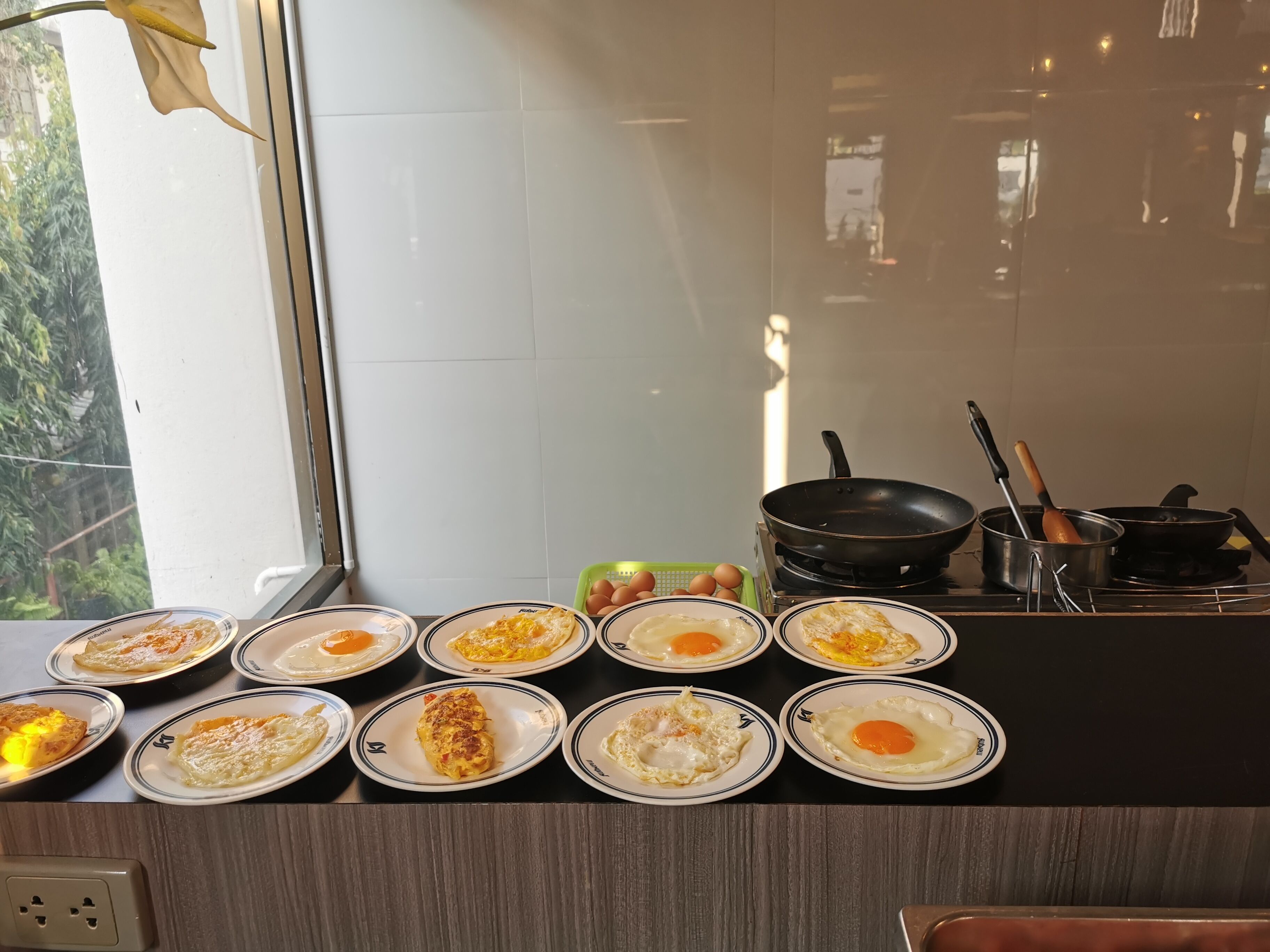A kitchen counter with multiple plates of fried eggs and a window in the background.