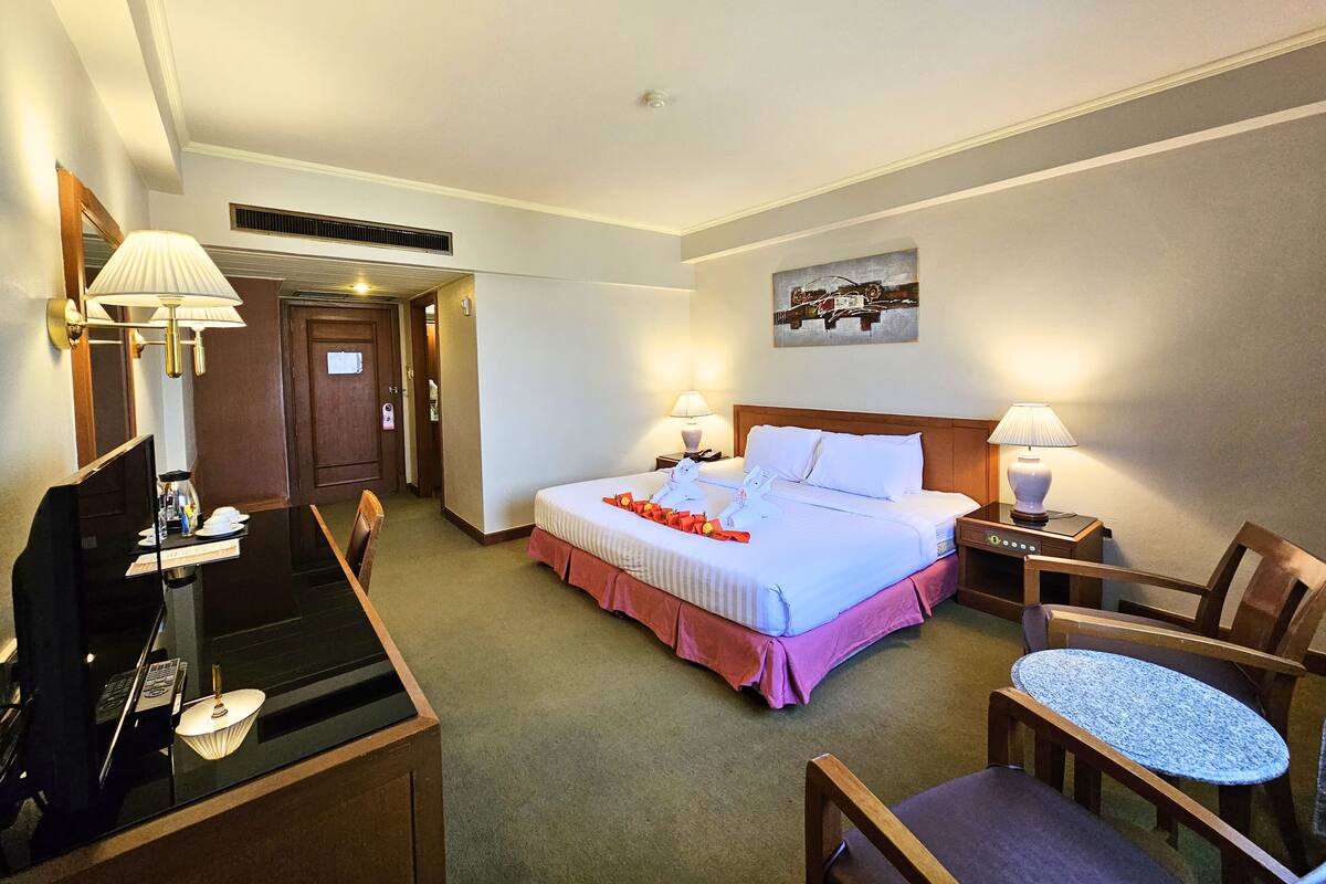 A hotel room with a bed, desk, chairs, and a painting on the wall.