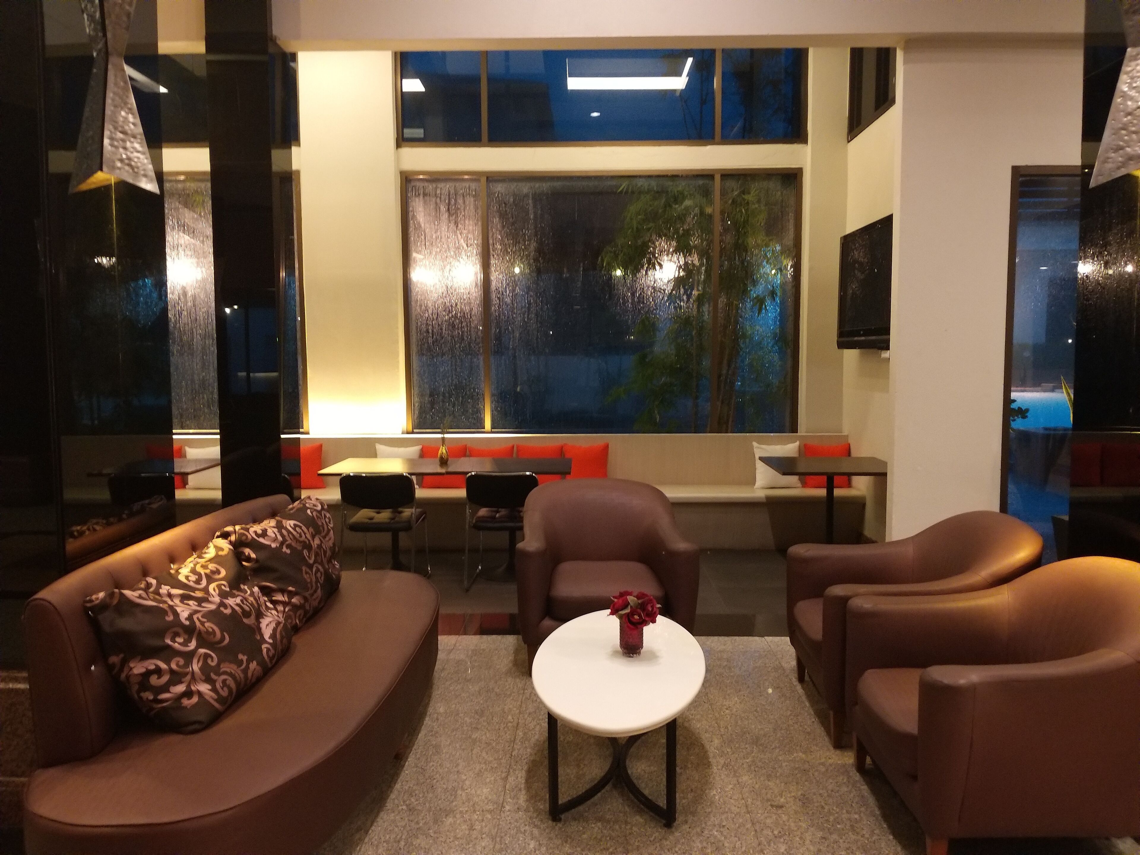 Een moderne woonkamer met een bank, stoelen, een bijzettafeltje en een groot raam met uitzicht op bomen.