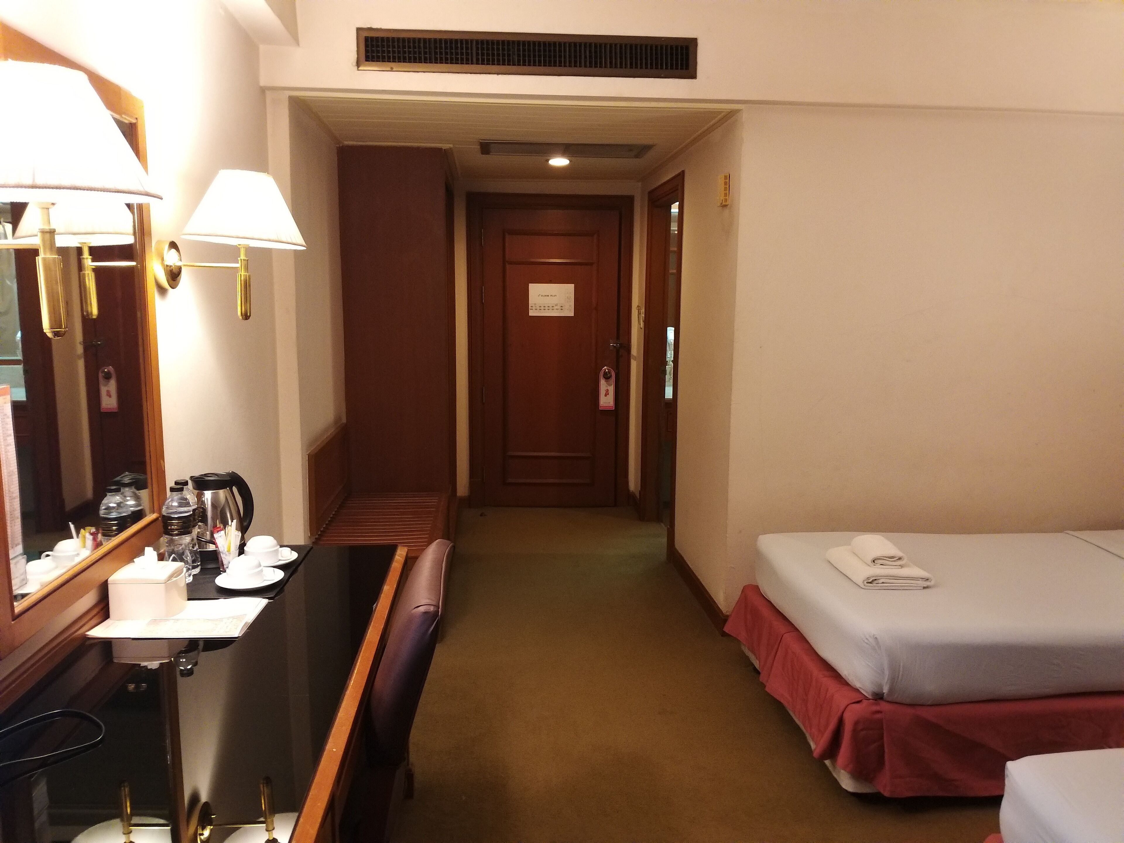 Ein Hotelzimmer mit Schreibtisch, zwei Betten, einem Spiegel und einer Tür zu einem Flur.