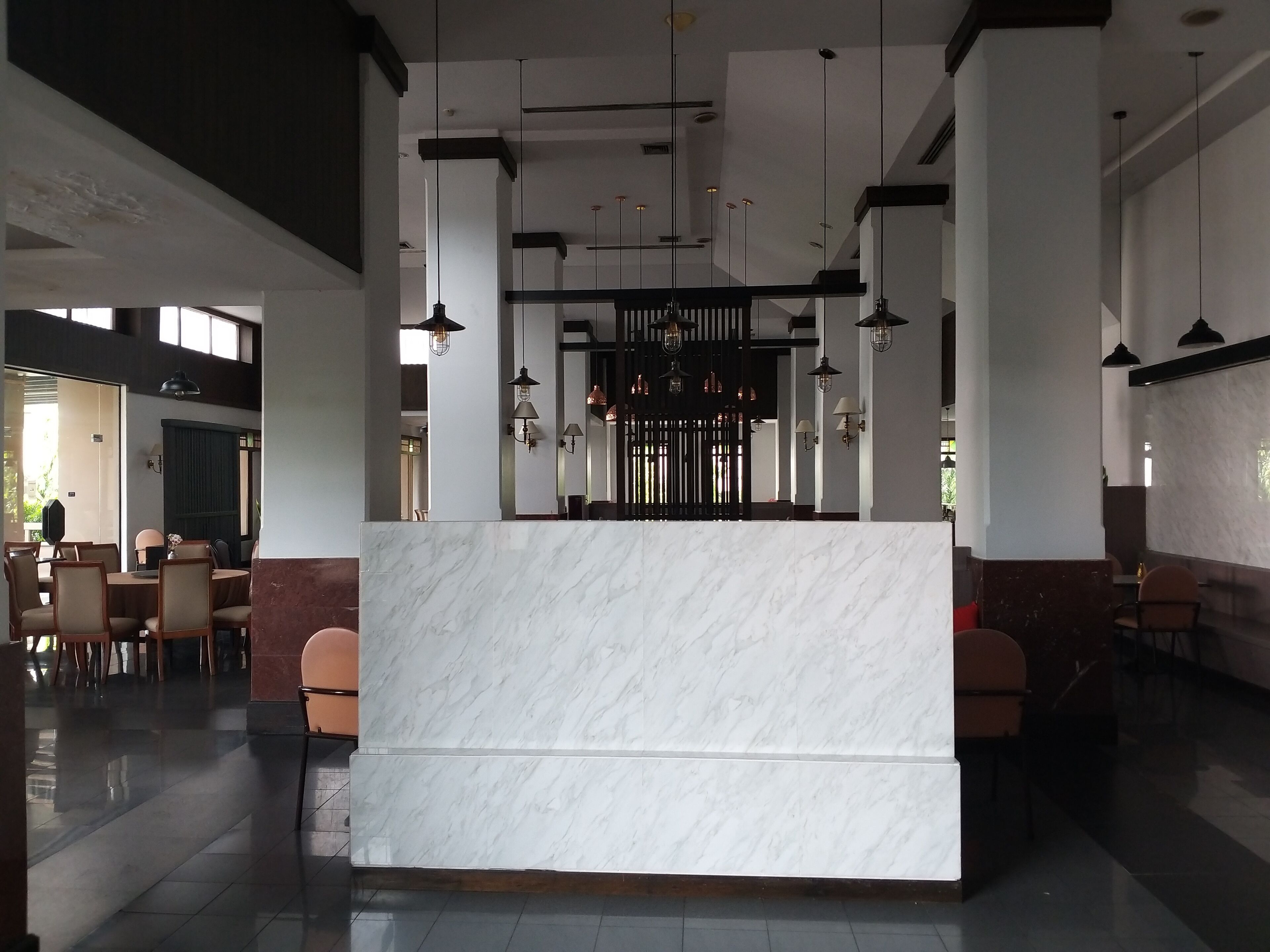 A modern reception area with a marble counter, pendant lighting, and a view of the adjacent dining area.