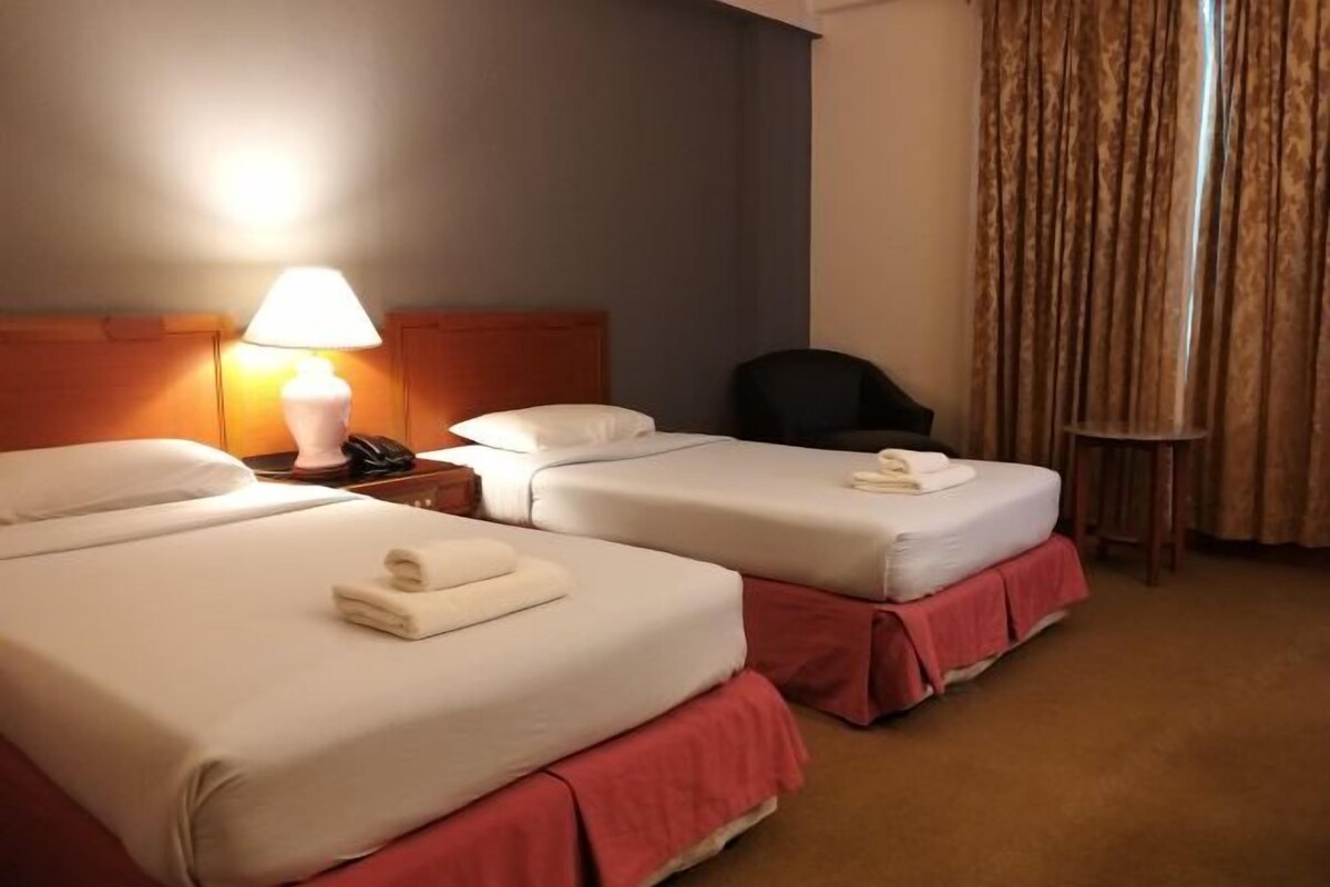 A hotel room with two beds, a nightstand with a lamp, a chair, and a small table.