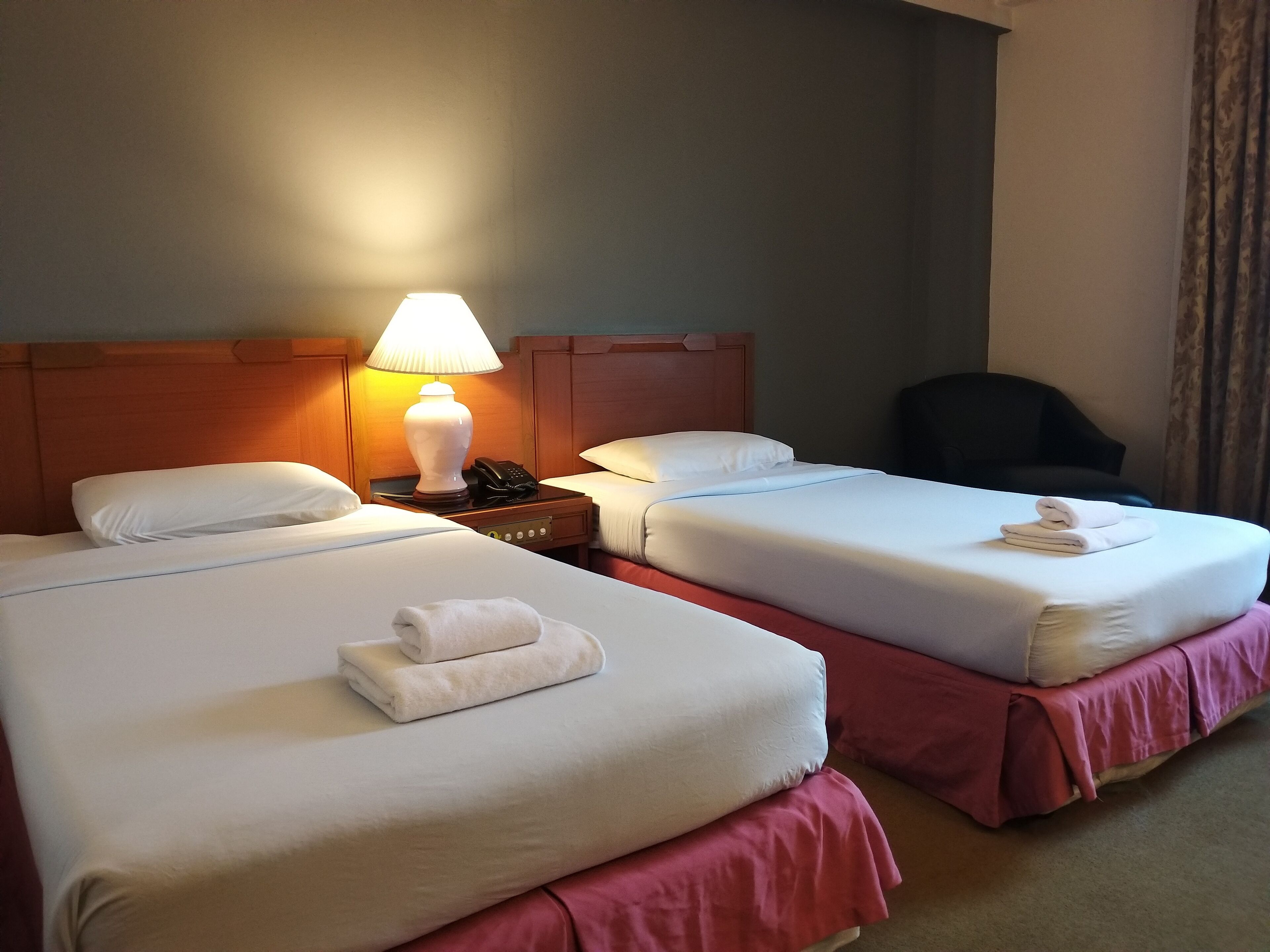 A hotel room with two beds, a nightstand with a lamp, a phone, and a chair.