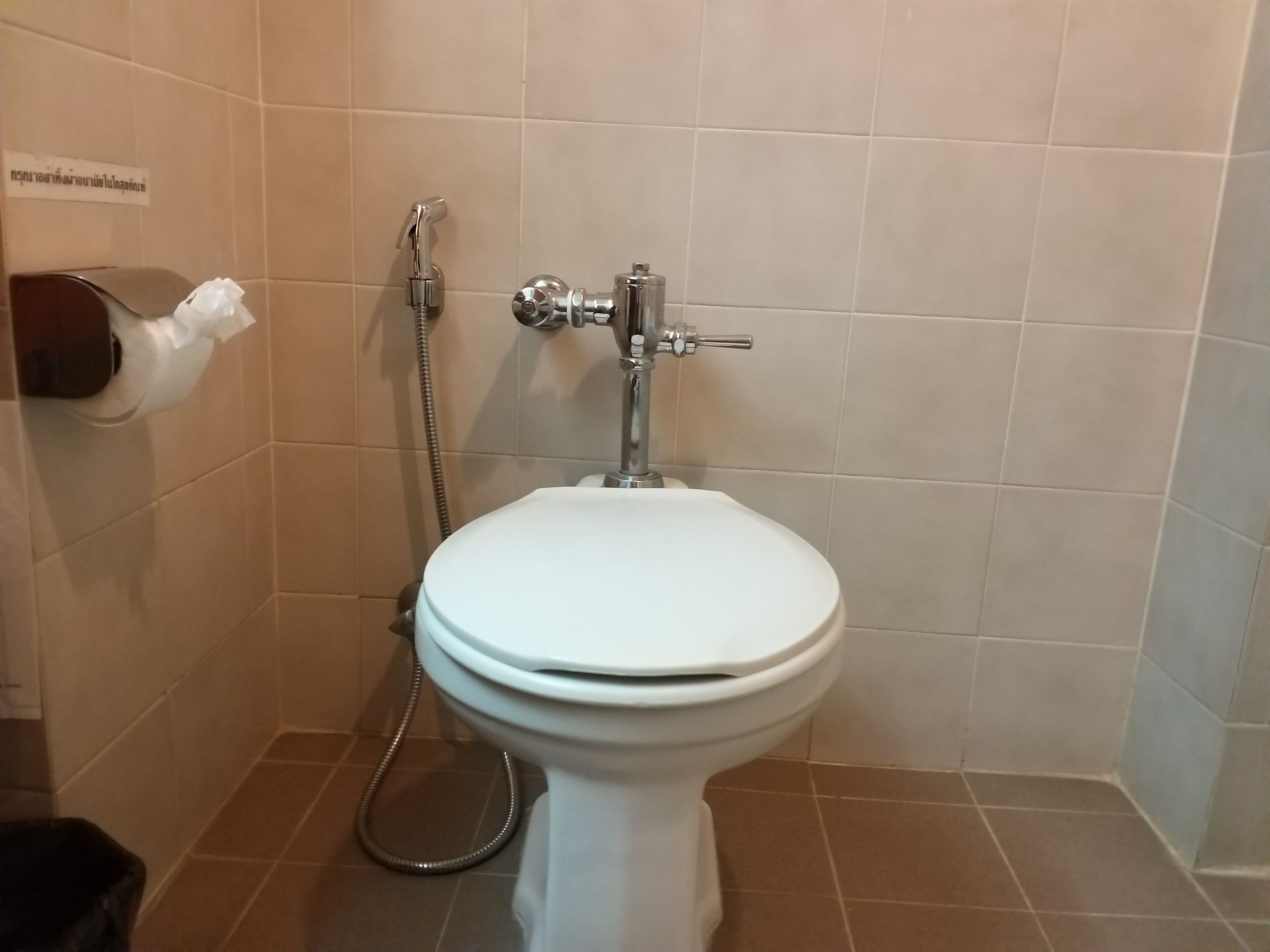 Un baño con inodoro blanco, dispensador de toallas de papel y cabezal de ducha.