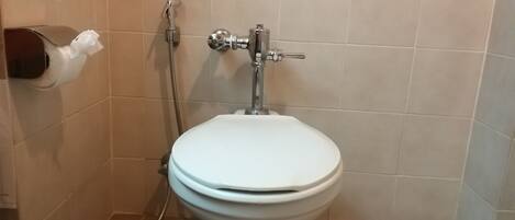 Un baño con inodoro blanco, dispensador de toallas de papel y cabezal de ducha.