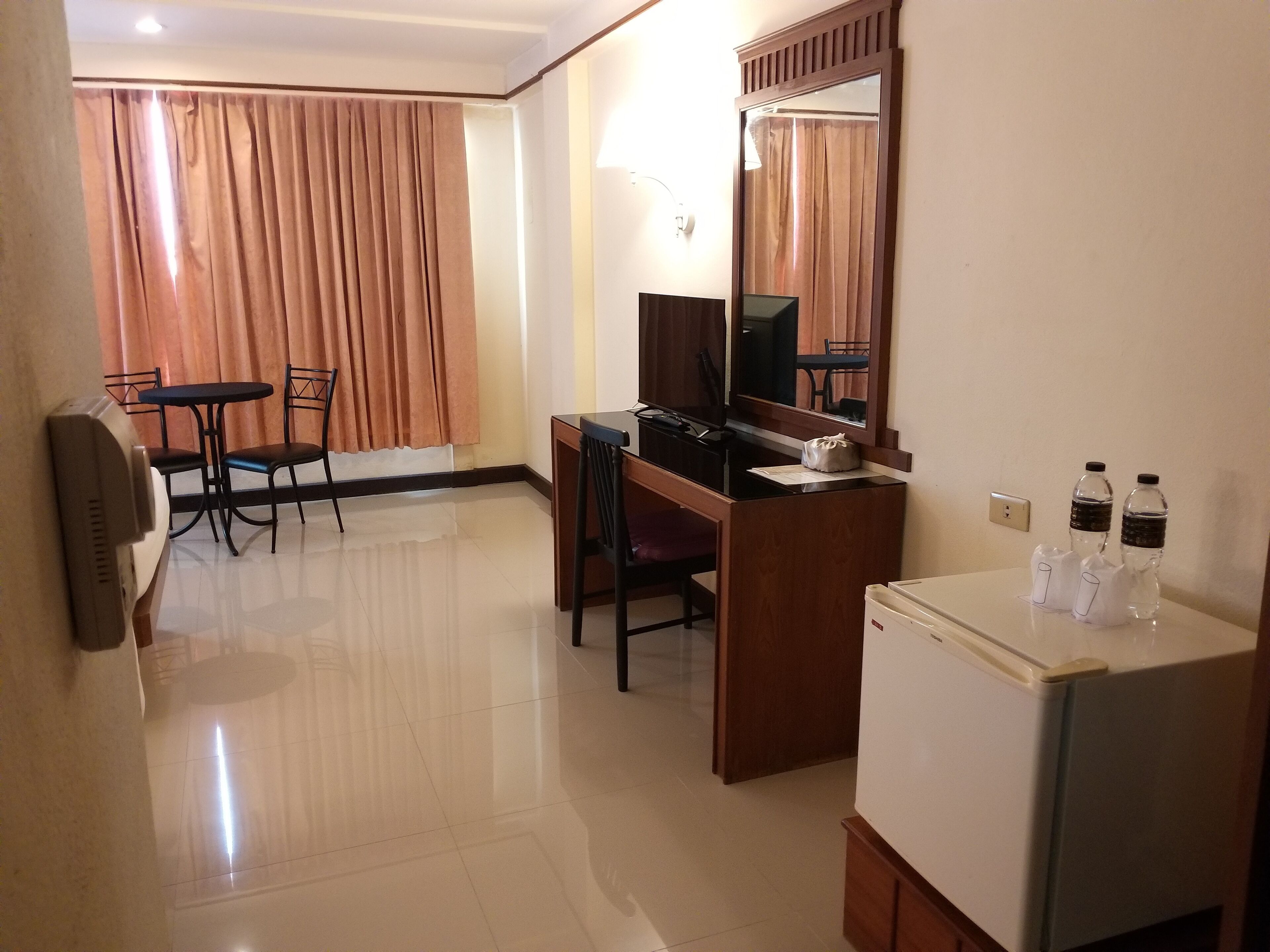 A hotel room with a desk, chair, television, and a refrigerator.