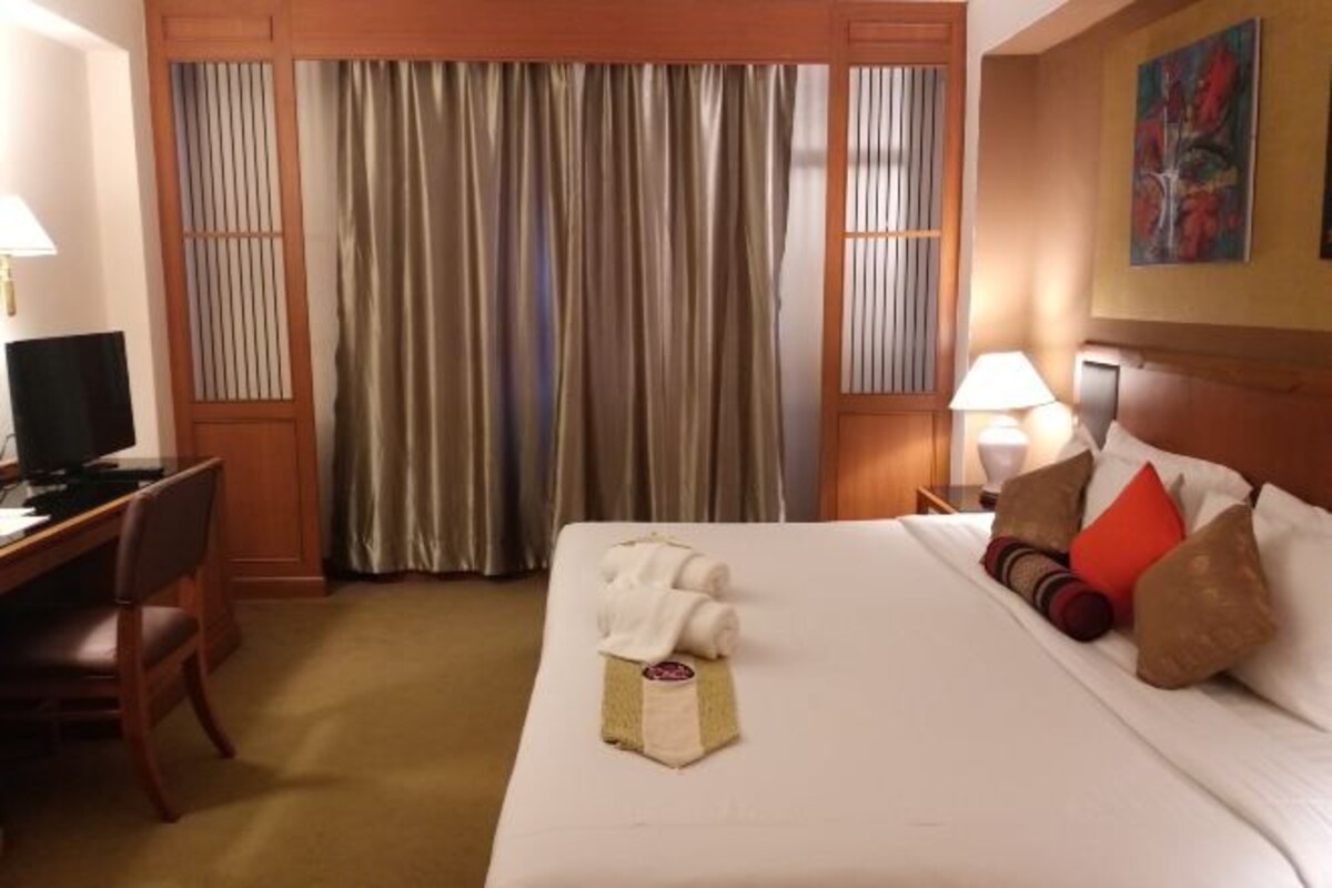 A hotel room with a bed, a desk, a chair, a television, a lamp, and a painting on the wall.
