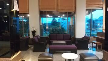 A modern living room with a sofa set, ottomans, and a small table. Large windows offer a view of the cityscape.