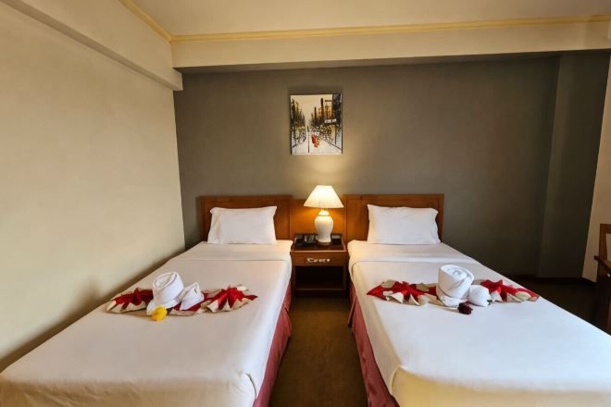 A hotel room with two single beds, a nightstand with a lamp, and a painting on the wall.