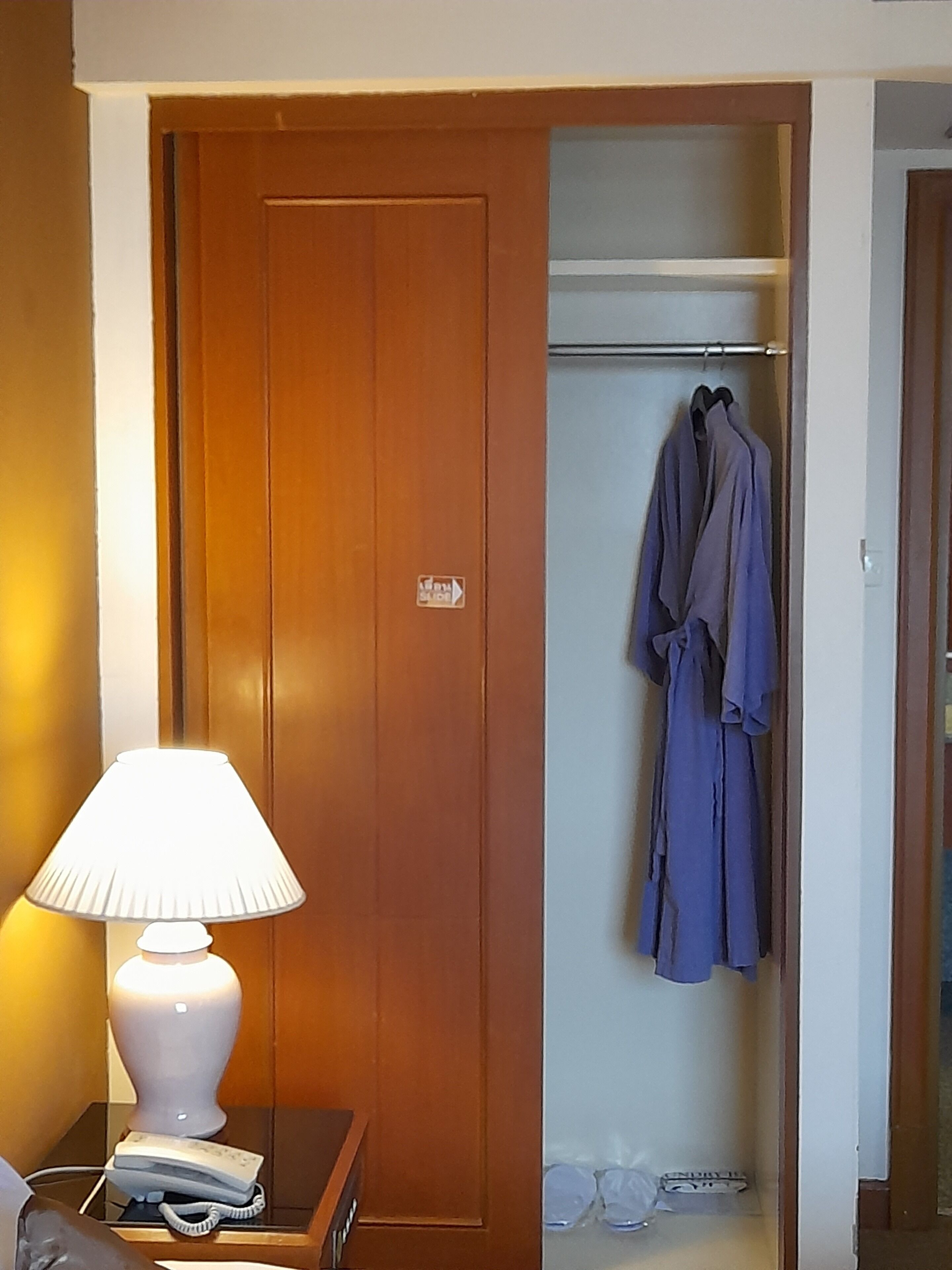 A wooden door with a sign, a lamp, and a robe hanging on a rack in a room.