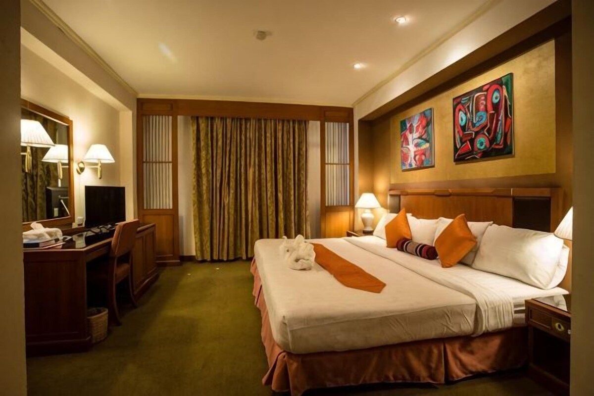 Une chambre d’hôtel avec un grand lit, un bureau avec un ordinateur, une chaise, une télévision et une fenêtre avec des rideaux.