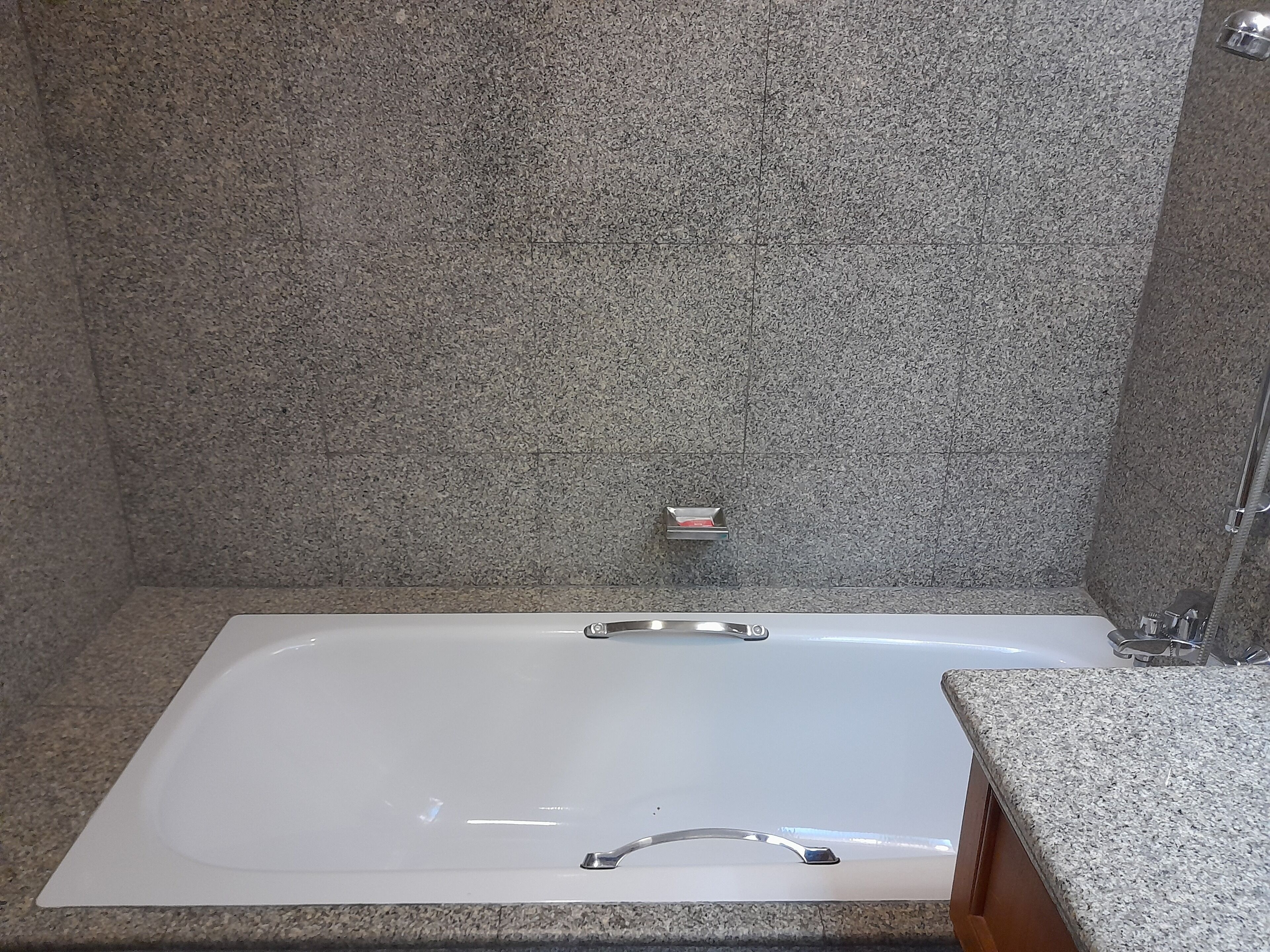 Une salle de bain avec une baignoire blanche, des murs en granit et un plan de toilette en granit.