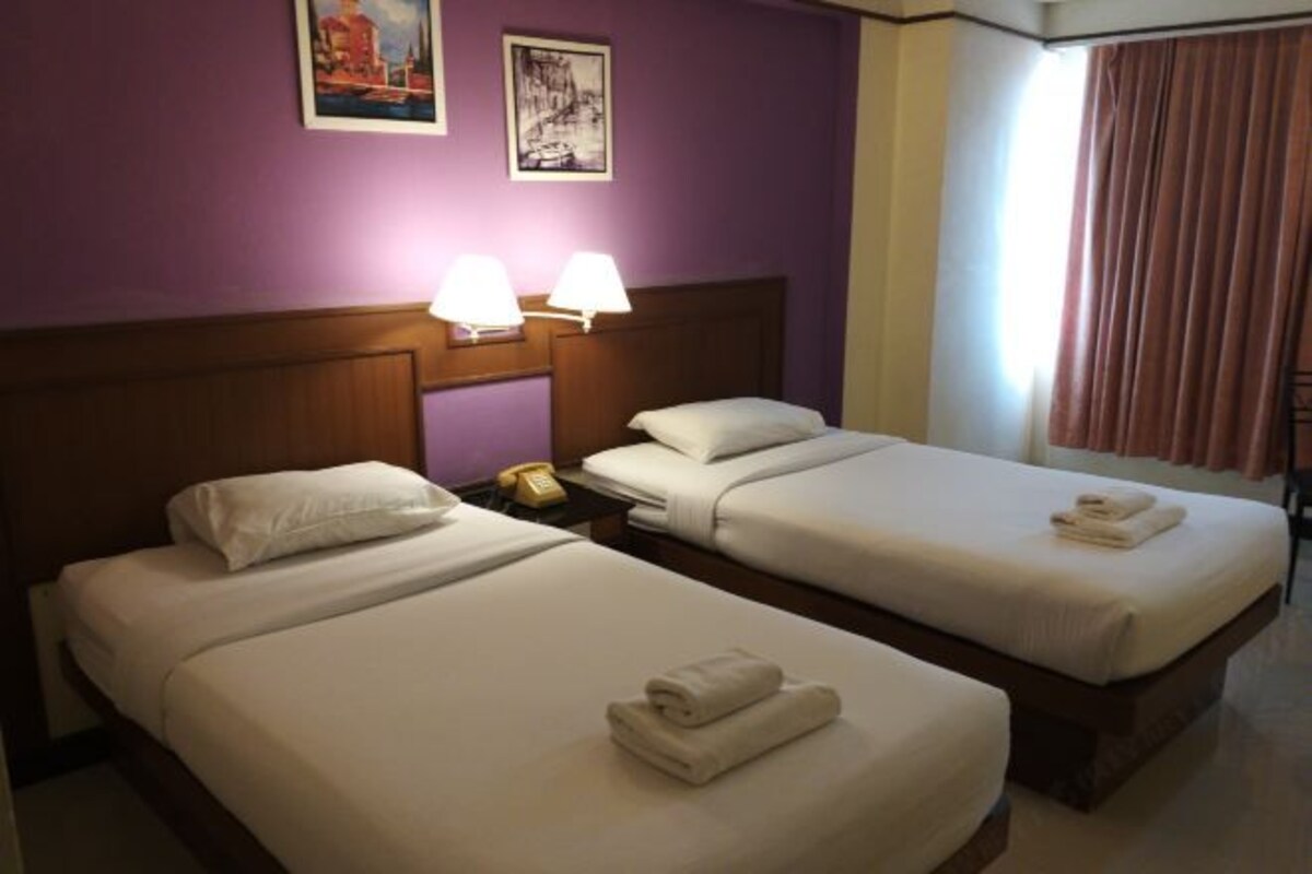 A hotel room with two single beds, a wooden headboard, two bedside lamps, and a telephone on the nightstand.
