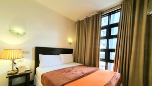 A hotel room with a bed, a nightstand, a lamp, a wall-mounted light, and a window with curtains. - A Hotel Baguio (Baguio)